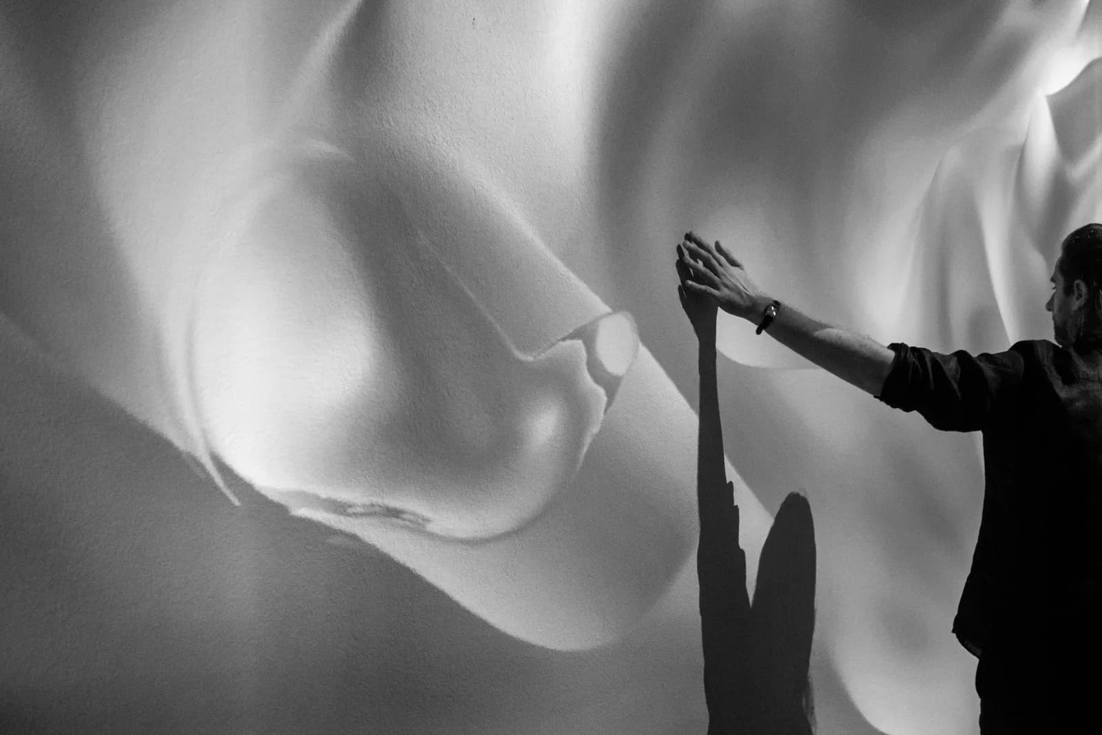 A person reaching toward projected light, casting a hand shadow on the wall.